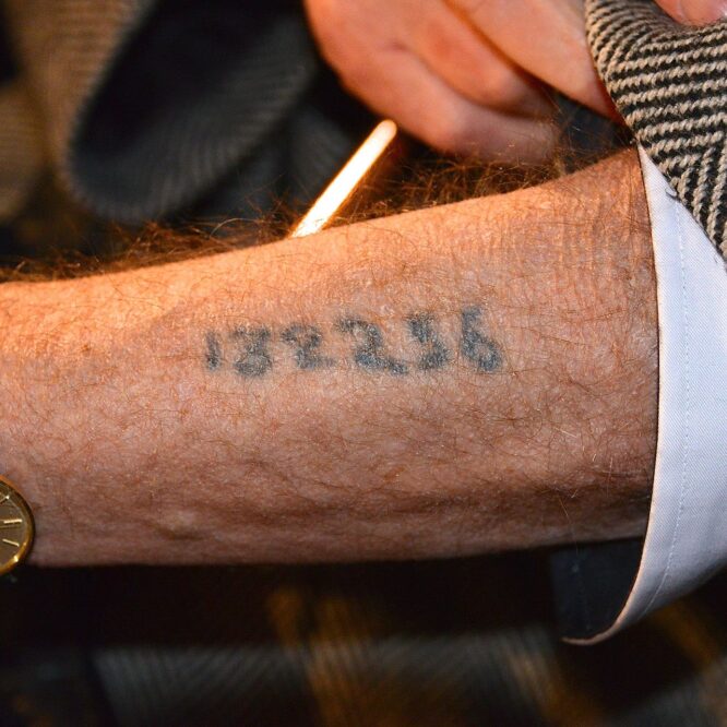 Holocaust survivor showing Auschwitz tattoo number on arm